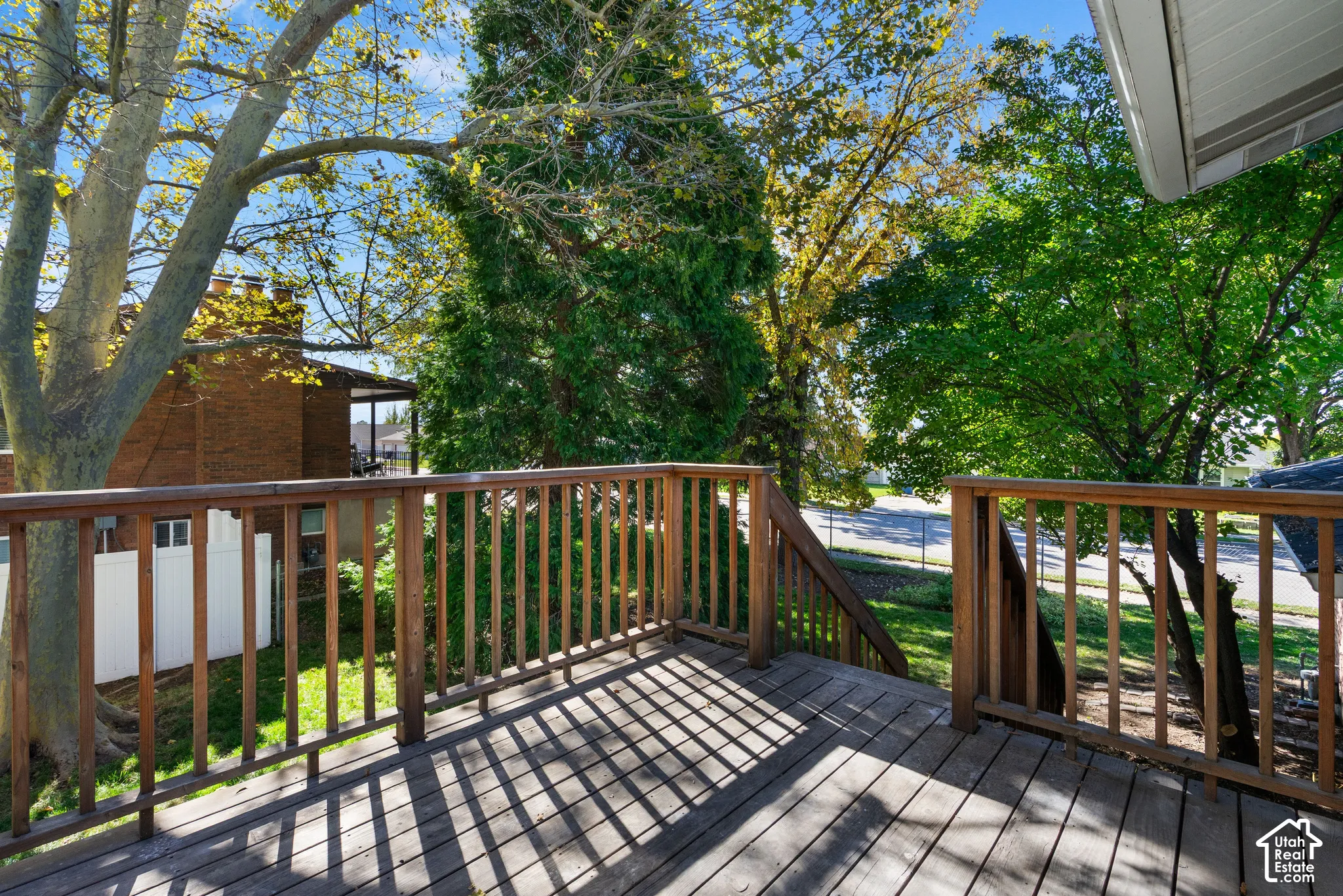 Elevated wooden deck featuring vertical balusters, a wooden staircase, and mature tree canopy coverage