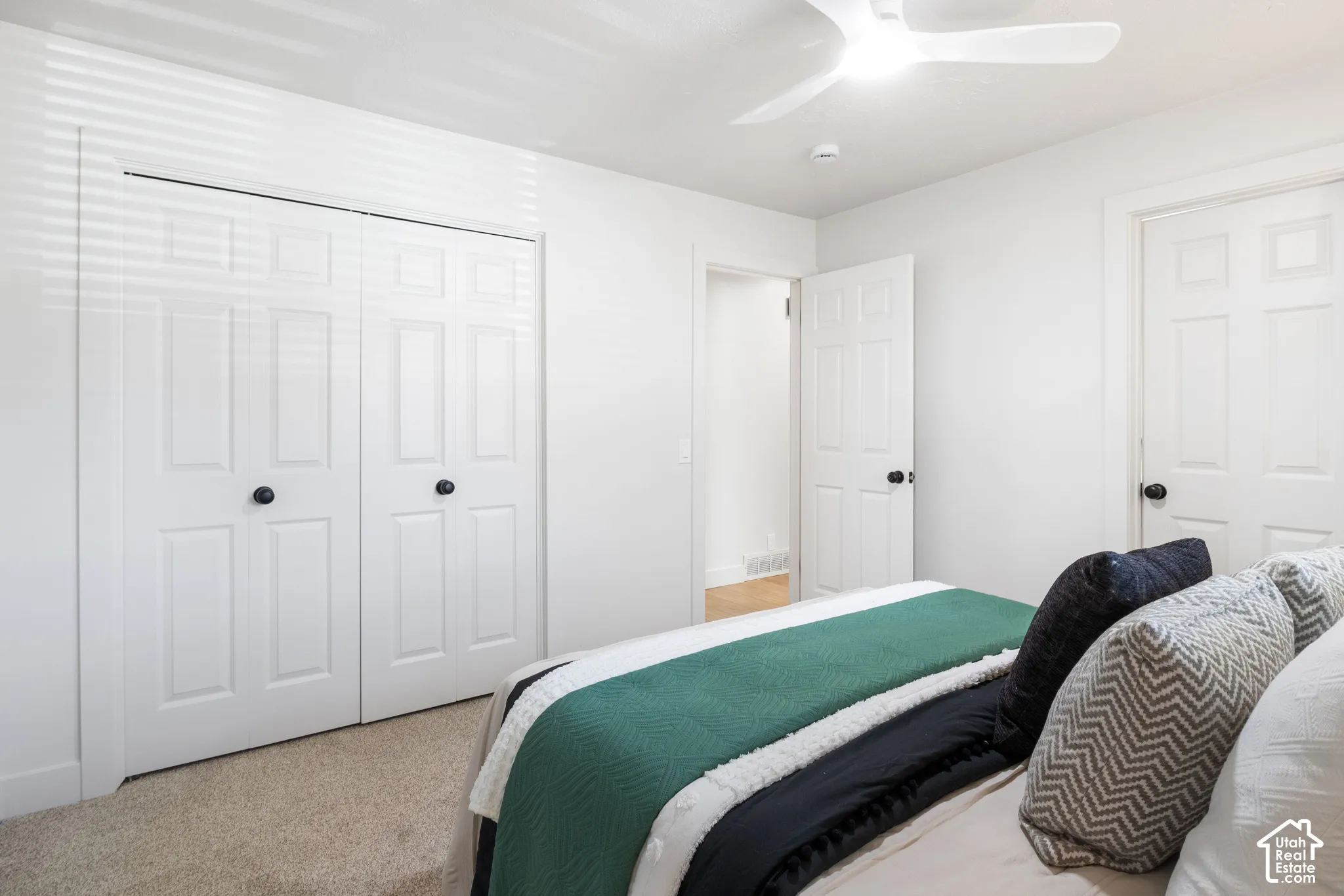 Room featuring carpeted flooring, white six-panel doors, dual-panel closet doors with matte black hardware, and an integrated ceiling fan