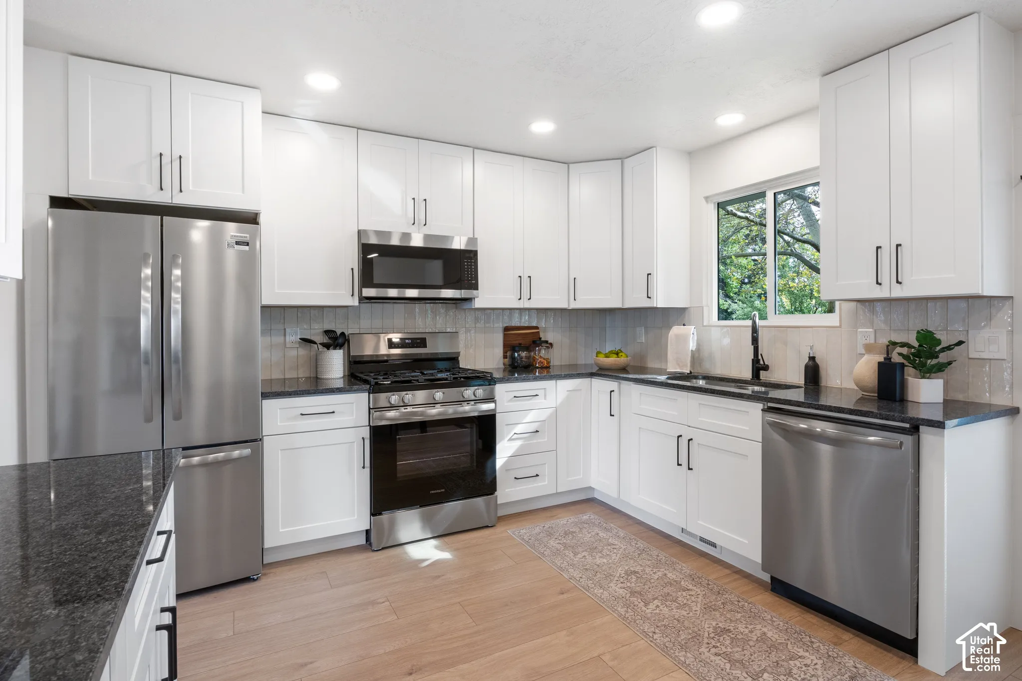 Kitchen featuring white shaker-style cabinetry, dark stone countertops, stainless steel appliances, wood-finish flooring, and recessed lighting