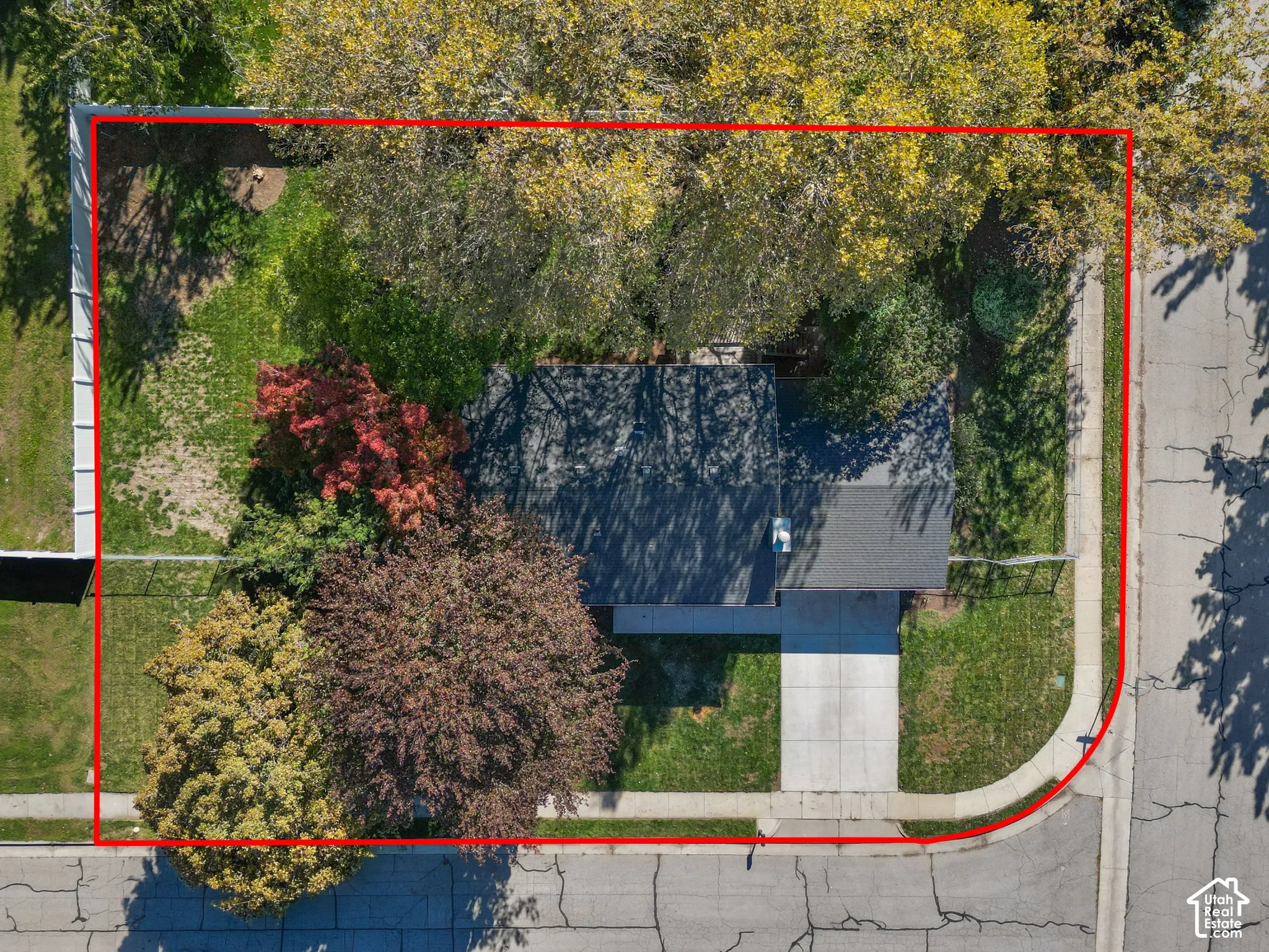 Corner lot featuring mature trees, a concrete driveway, a grass lawn, and a fenced perimeter