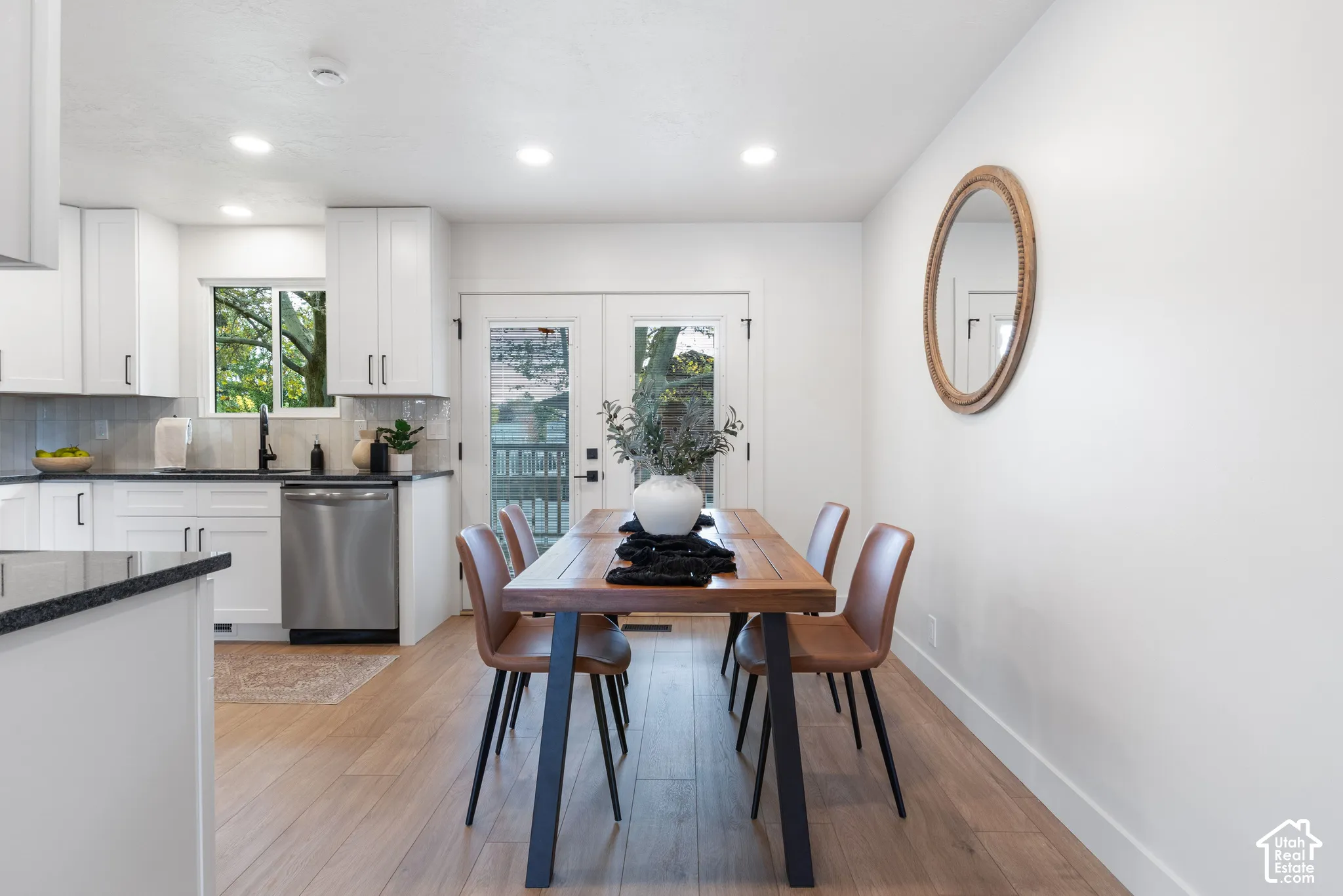 Kitchen featuring white shaker-style cabinetry, dark stone countertops, stainless steel dishwasher, wood-finish flooring, and double glass-pane doors