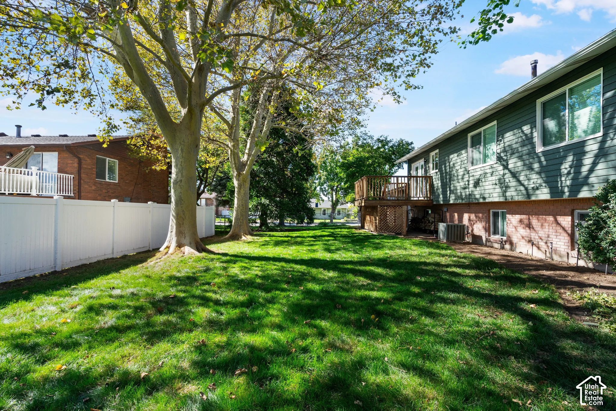 Rear yard featuring a grass lawn, white vinyl privacy fencing, mature trees, and an elevated wood deck