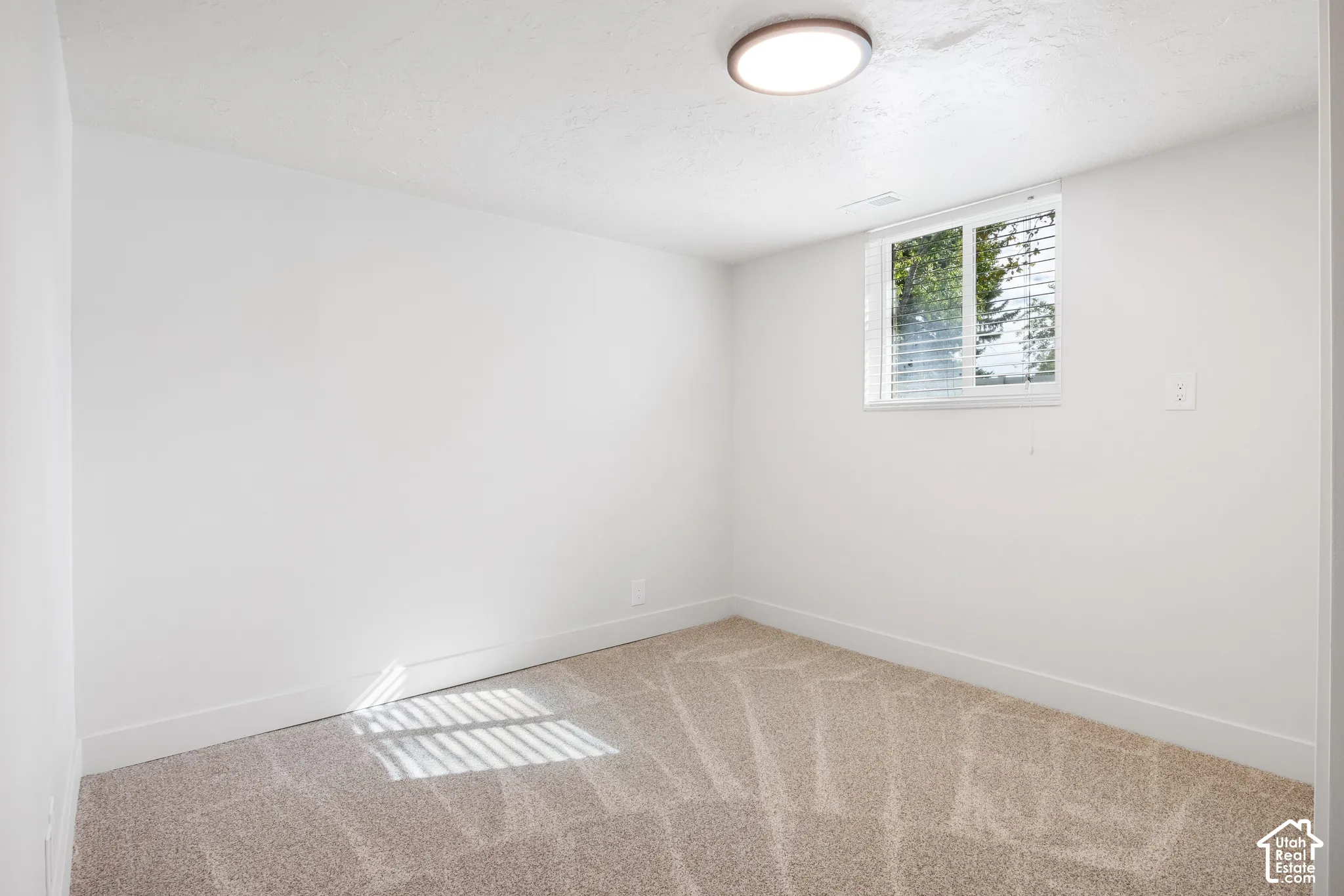 Neutral-toned wall-to-wall carpeting, crisp white walls, and a recessed ceiling light fixture, featuring a sliding window with horizontal blinds