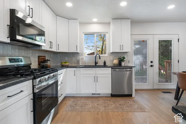 Kitchen featuring white shaker-style cabinetry, stainless steel appliances, dark stone countertops, recessed lighting, and wood-finish flooring