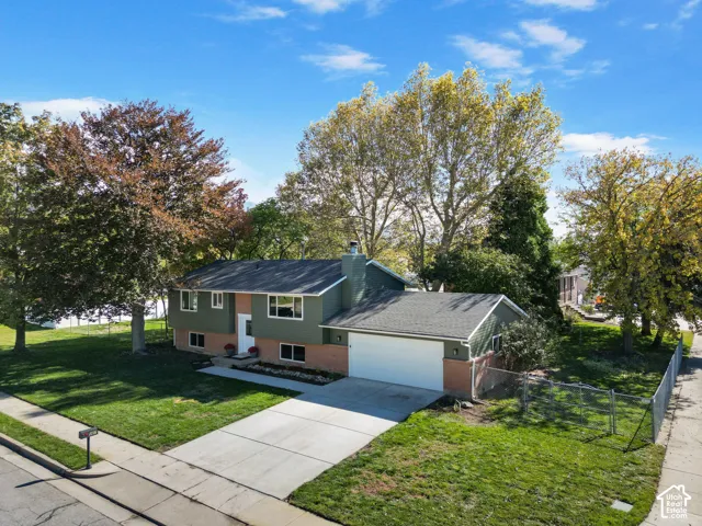 Split-level exterior featuring a brick and siding facade, an attached two-car garage, an asphalt shingle roof, and an expansive lawn with mature trees