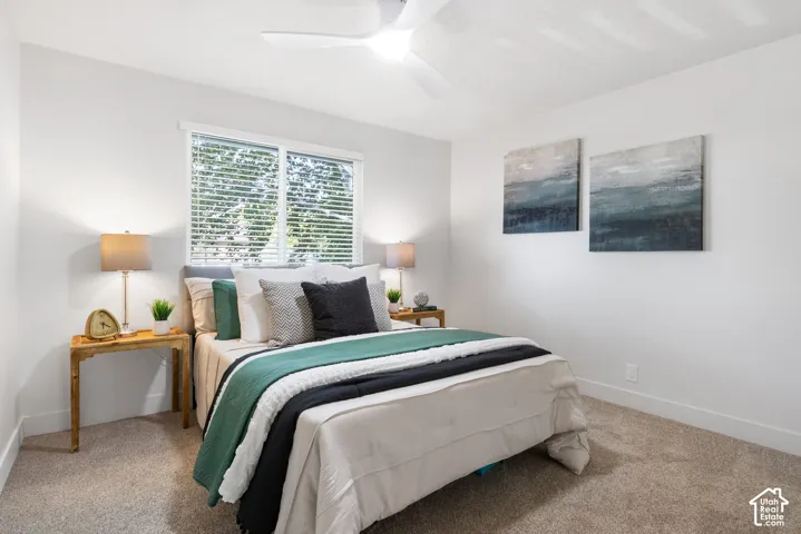 Neutral-toned interior space featuring neutral wall paint, carpeted flooring, a multi-blade ceiling fan, and a large window with horizontal blinds