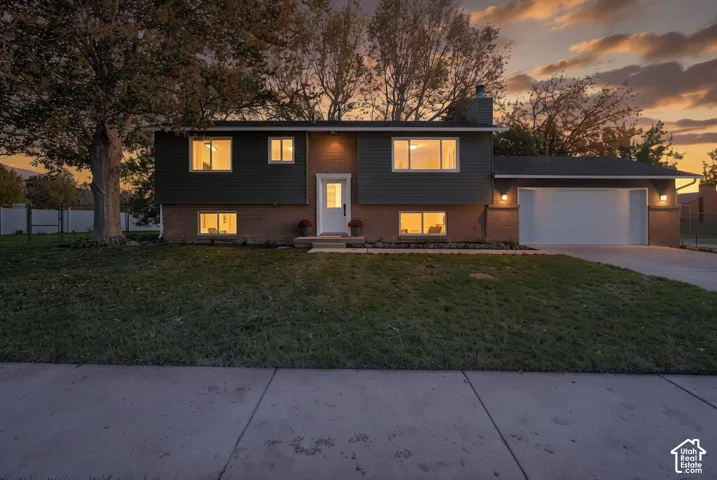 Split-level exterior featuring a brick and horizontal siding facade, attached two-car garage, concrete driveway, and mature landscaping