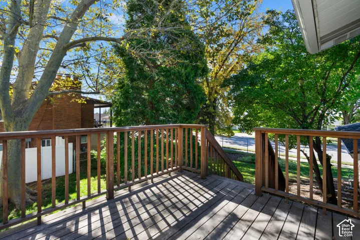 Elevated wooden deck featuring vertical balusters, a wooden staircase, and mature tree canopy coverage