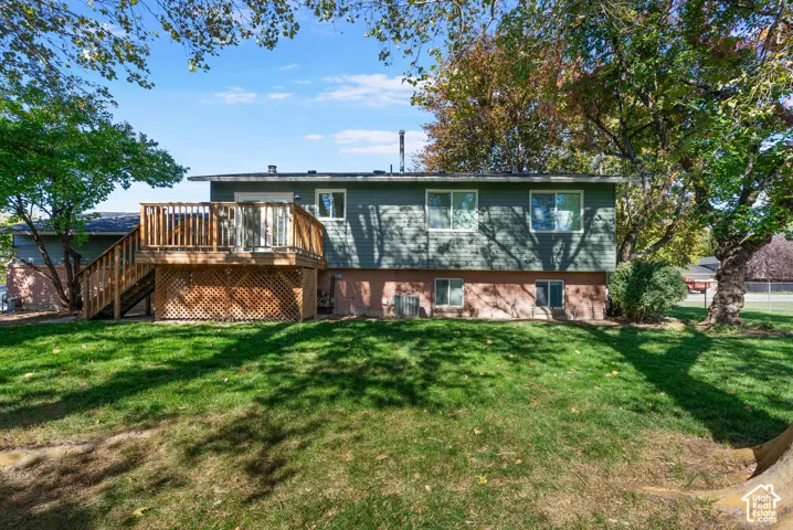 Rear exterior featuring a wood deck with lattice skirting, brick and horizontal siding, mature trees, and a lawn