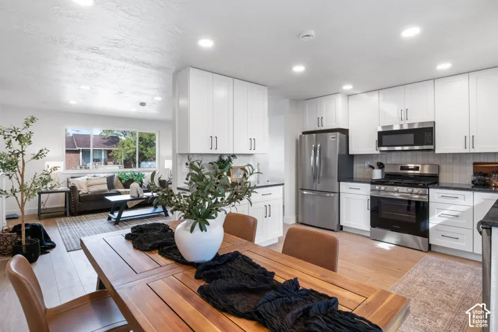 Kitchen featuring white shaker cabinetry, stainless steel appliances, dark countertops, recessed lighting, and wood-finish flooring