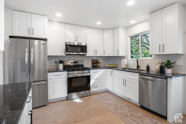 Kitchen featuring white shaker-style cabinetry, dark stone countertops, stainless steel appliances, wood-finish flooring, and recessed lighting
