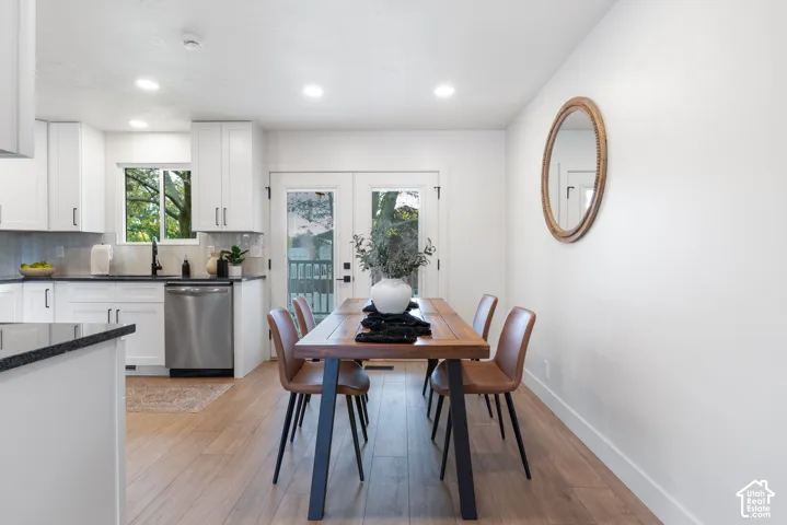 Kitchen featuring white shaker-style cabinetry, dark stone countertops, stainless steel dishwasher, wood-finish flooring, and double glass-pane doors