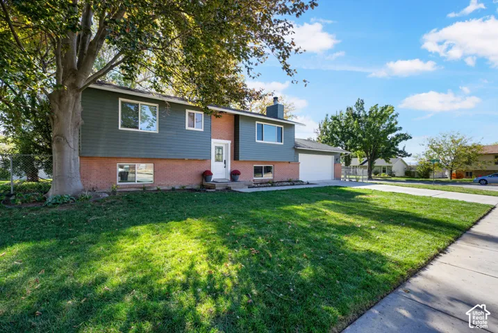 Split-level exterior featuring a brick and horizontal siding facade, attached two-car garage, concrete driveway, and mature landscaping