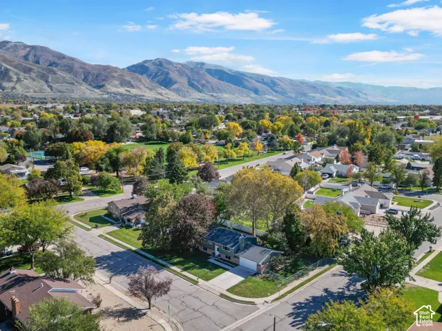 Aerial perspective featuring a residential property with a two-car garage, concrete driveway, mature trees, and prominent mountain backdrops