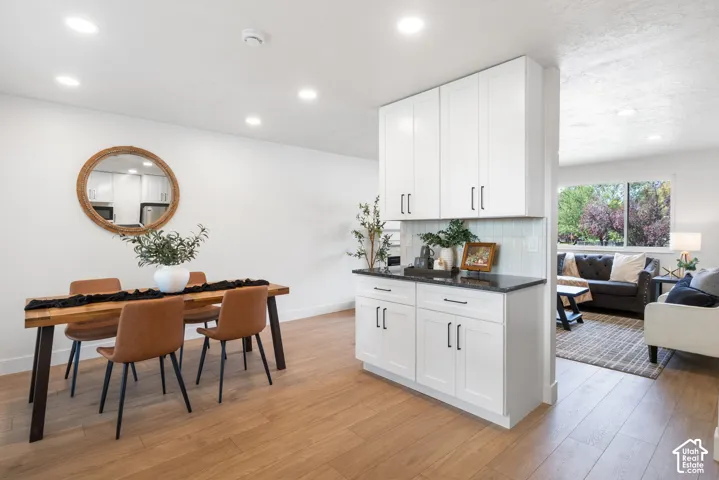Custom cabinetry with matte black hardware, stone-surface countertop, subway tile backsplash, recessed lighting, and wood-finish flooring