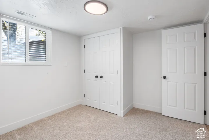 Room featuring neutral carpeting, double-door closet with round hardware, six-panel interior door, and natural light from a window with horizontal blinds