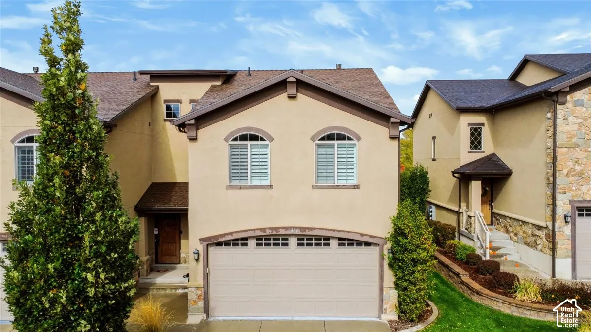 Stucco exterior featuring an arched-panel garage door, stacked-stone accents, tiered hardscaping, and dual-pane windows with integrated shutters