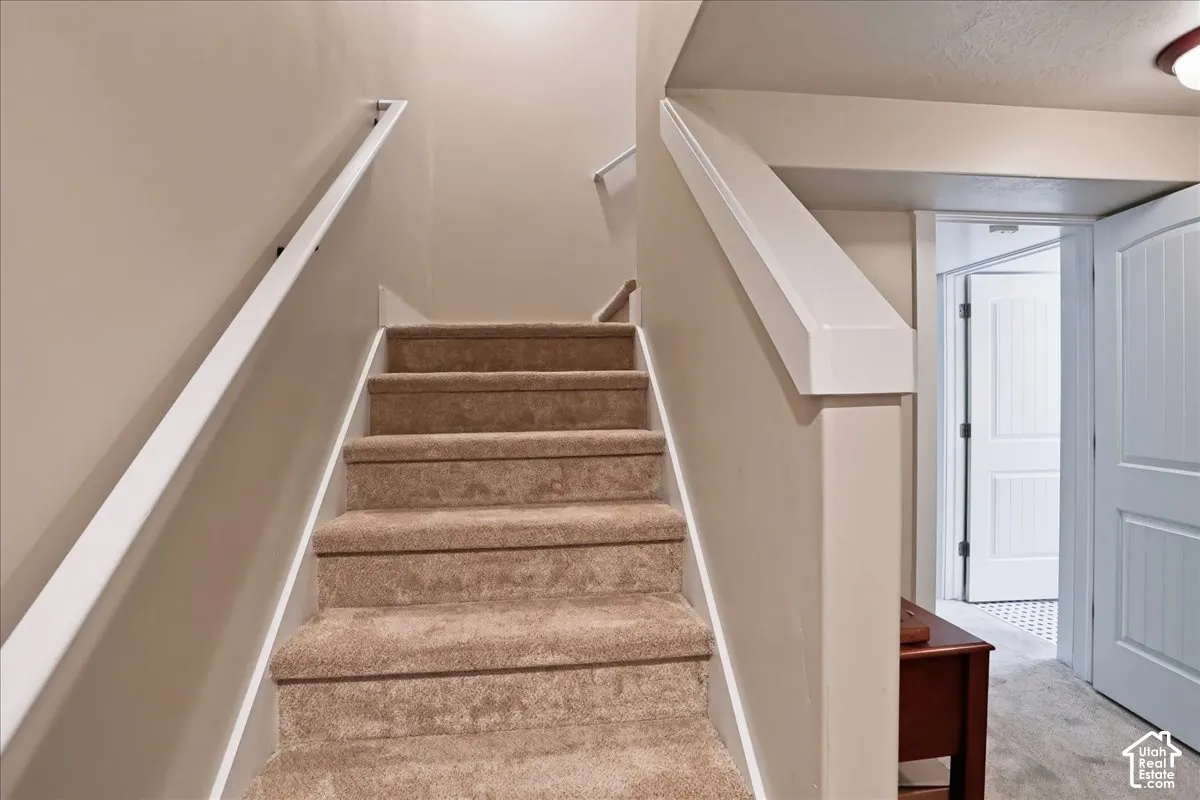 Staircase featuring wall-to-wall carpeting, white handrails, and neutral wall paint