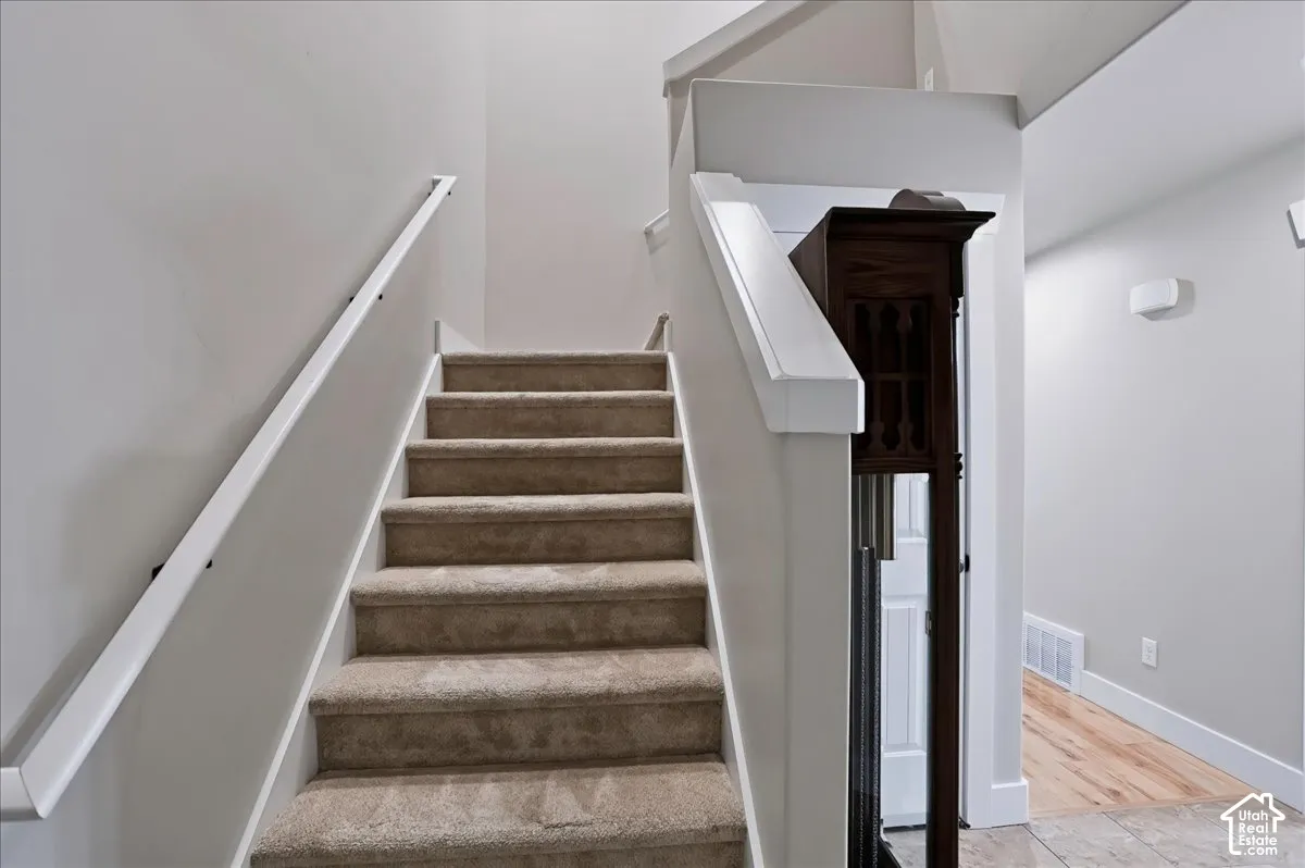 Staircase featuring neutral carpeted treads, white handrails, and wood-finish flooring in the hallway