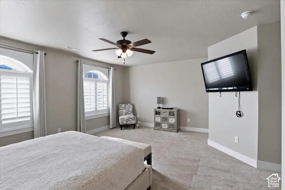 Master Suite featuring wall-to-wall carpeting, two windows with arched transoms and plantation shutters, and a ceiling fan with integrated lighting