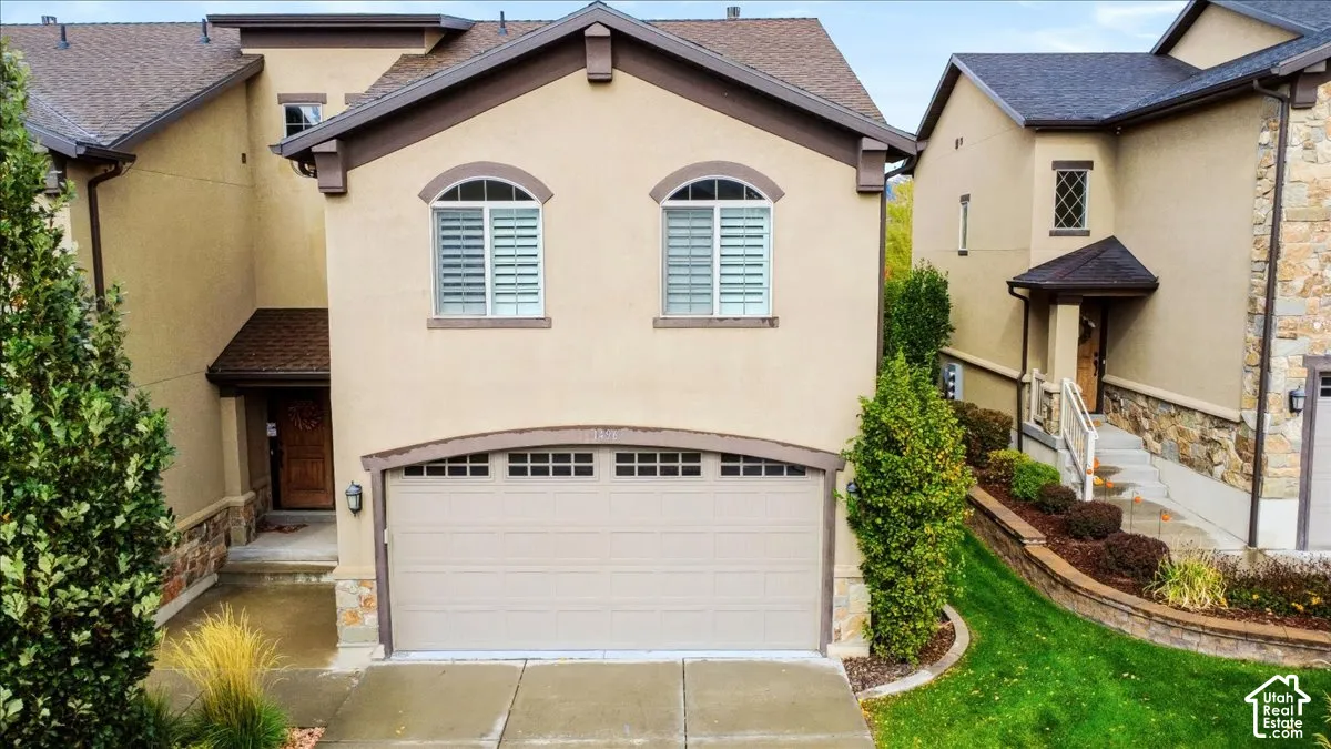 Stucco exterior featuring arched-top windows, multi-pane garage door, stone masonry accents, and concrete driveway