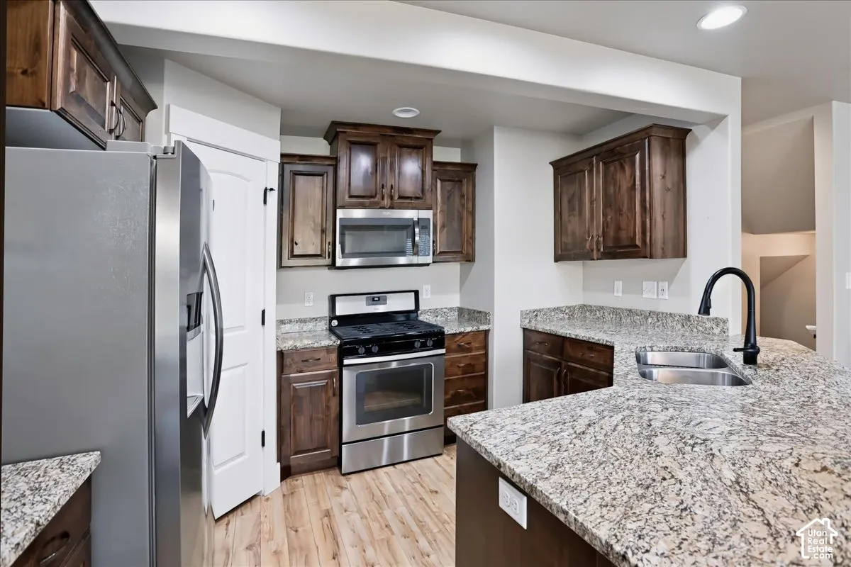 Kitchen featuring dark wood-finish cabinetry, stone-surface countertops, stainless steel appliances, pantry, a peninsula with an undermount dual-basin sink, and matte black plumbing fixtures