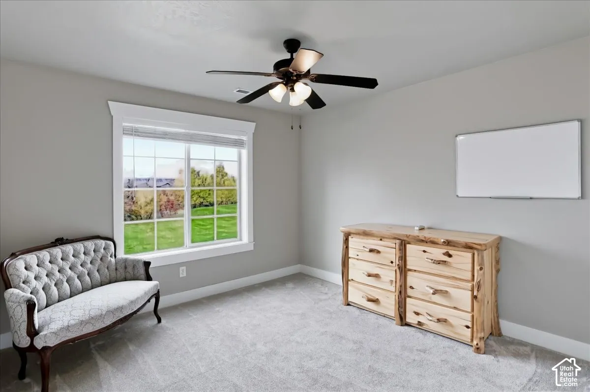 Neutral-toned room featuring wall-to-wall carpeting, a multi-pane window with custom trim, and a ceiling fan with integrated lighting