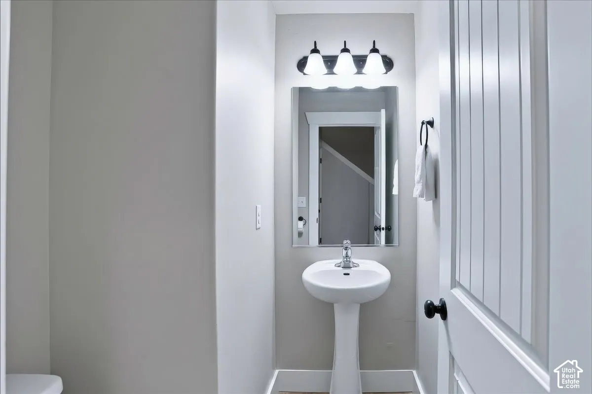 Powder Room with White pedestal sink with a chrome single-handle faucet, rectangular wall mirror, and three-light fixture featuring frosted glass shades