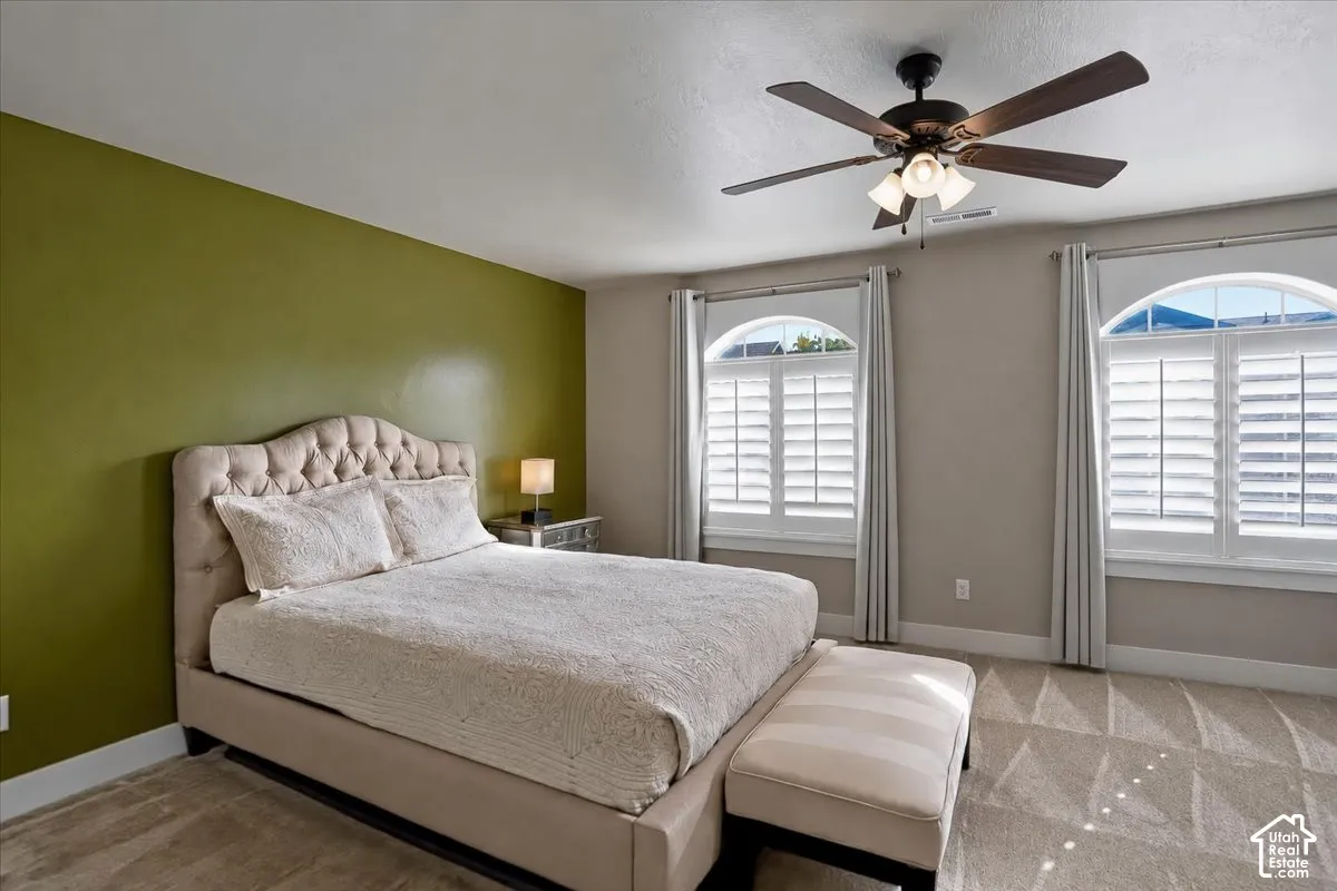 Primary Suite featuring two Southern Exposure windows with arched transits, interior plantation shutters, and a ceiling fan with integrated lighting
