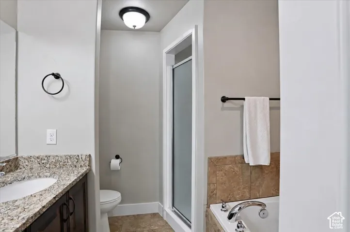 Primary Suite Bathroom featuring a stone-patterned countertop with integrated sink, dark wood-finish cabinetry, a glass-enclosed shower, a soaking tub with tile surround, and matte black fixtures