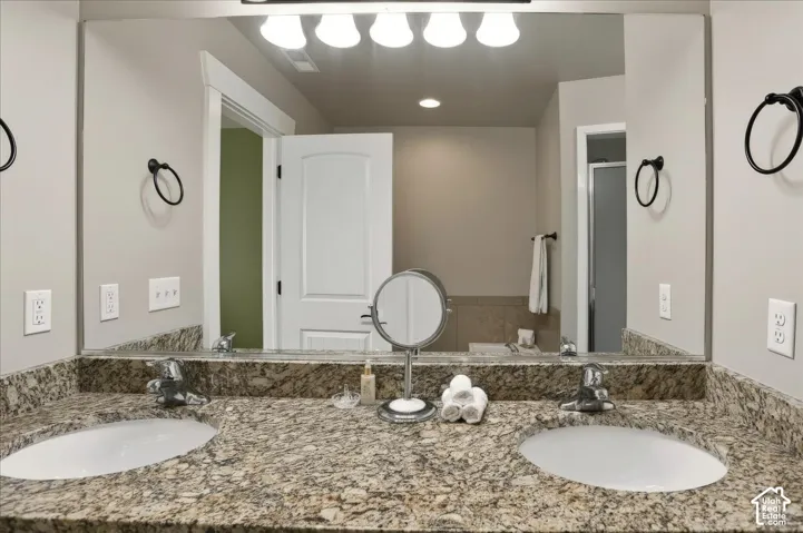 Mater Bath with Dual-sink vanity featuring a stone countertop, under-mount sinks, chrome widespread faucets, and an expansive wall-mounted mirror