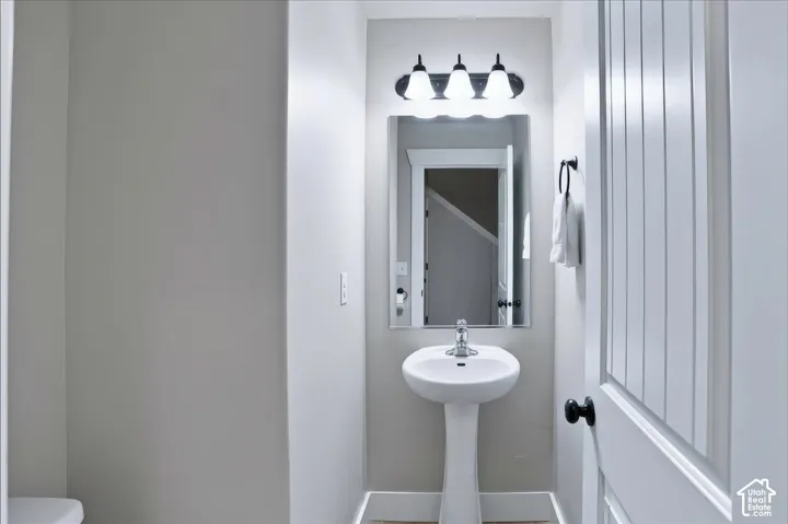 Powder Room with White pedestal sink with a chrome single-handle faucet, rectangular wall mirror, and three-light fixture featuring frosted glass shades