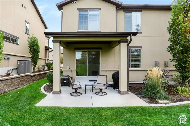 Stucco exterior featuring a covered concrete patio with square pillars, sliding glass door, and a manicured lawn with landscape curbing