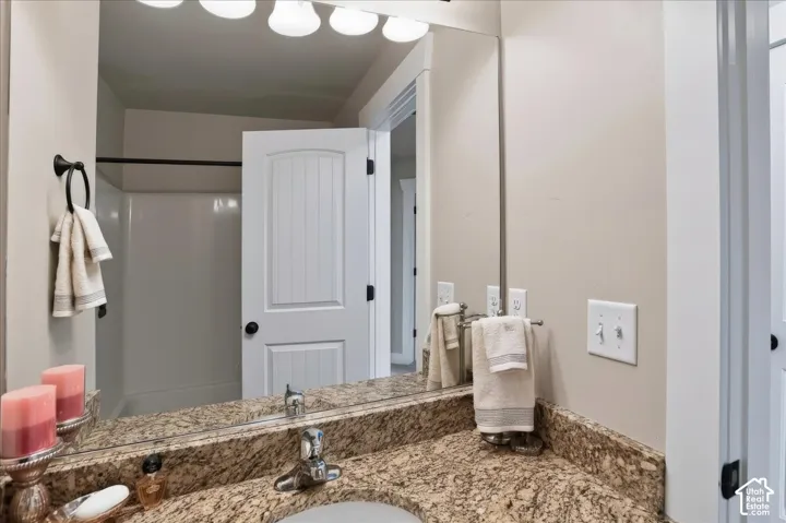 Stone-surfaced vanity countertop with an integrated basin, wall-mounted full-width mirror, multi-bulb overhead vanity lighting, and arched-panel interior door