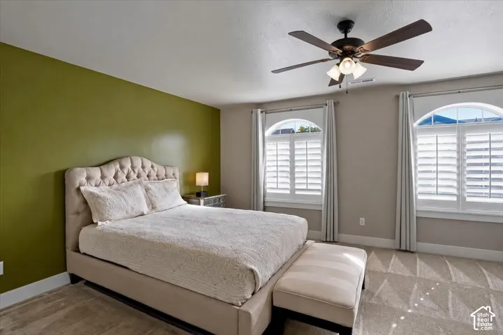 Primary Suite featuring two Southern Exposure windows with arched transits, interior plantation shutters, and a ceiling fan with integrated lighting