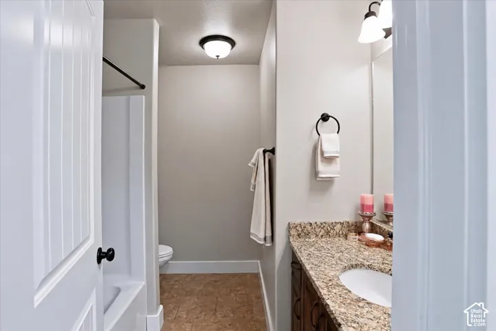 Primary Suite Bathroom featuring a stone-patterned vanity countertop, integrated sink, dark-finish cabinetry, built-in tub-shower combination, and matte black hardware