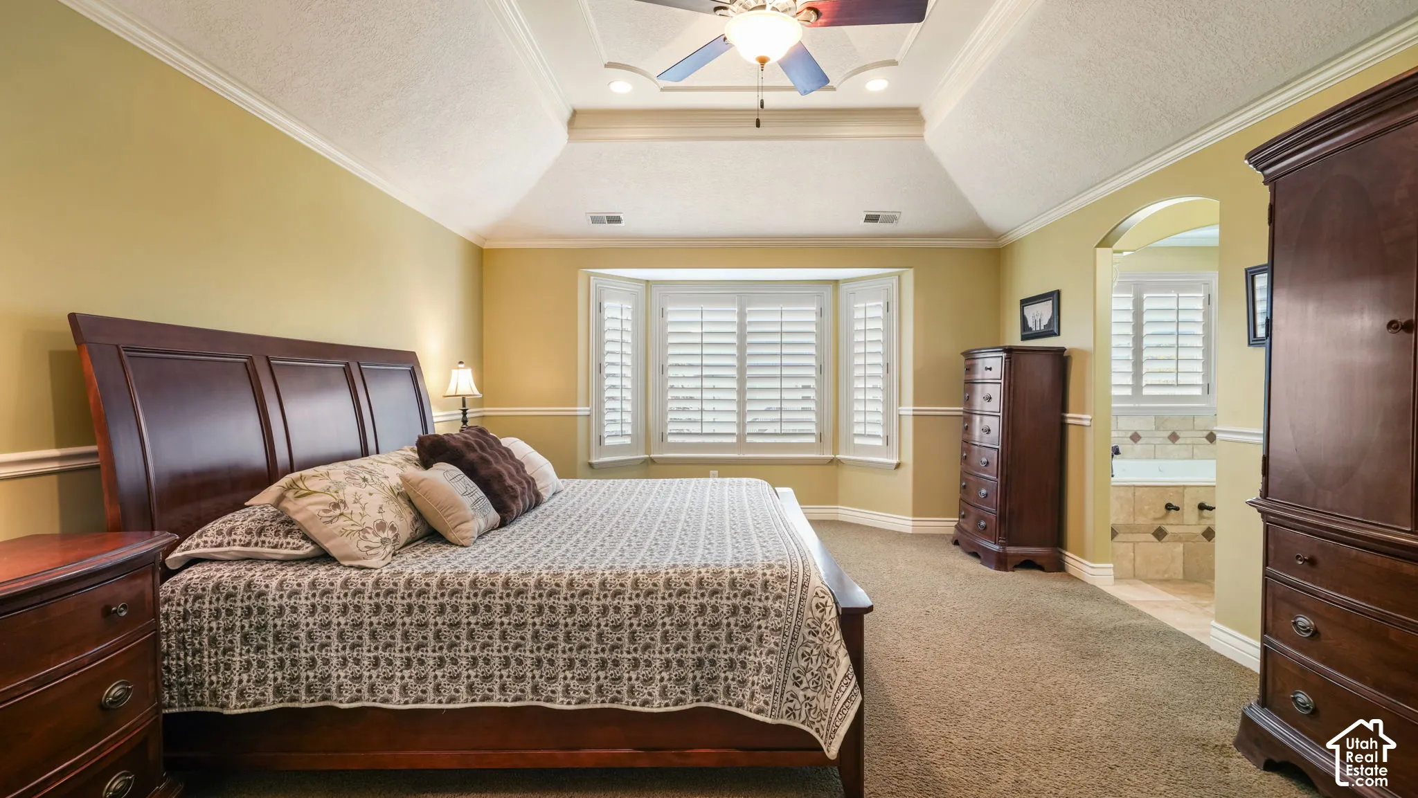 Tray ceiling with recessed lighting, bay window featuring plantation shutters, crown molding, and chair rail detailing