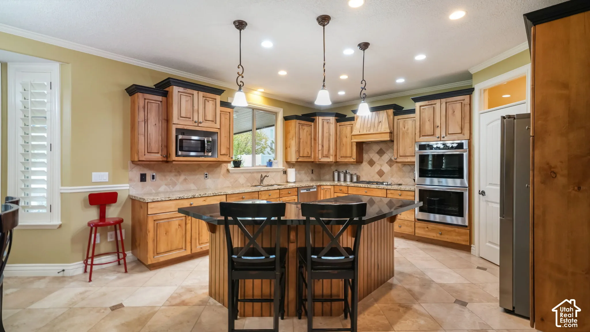 Kitchen featuring custom wood cabinetry, stone countertops, a multi-tiered center island, stainless steel double wall ovens, and tile flooring