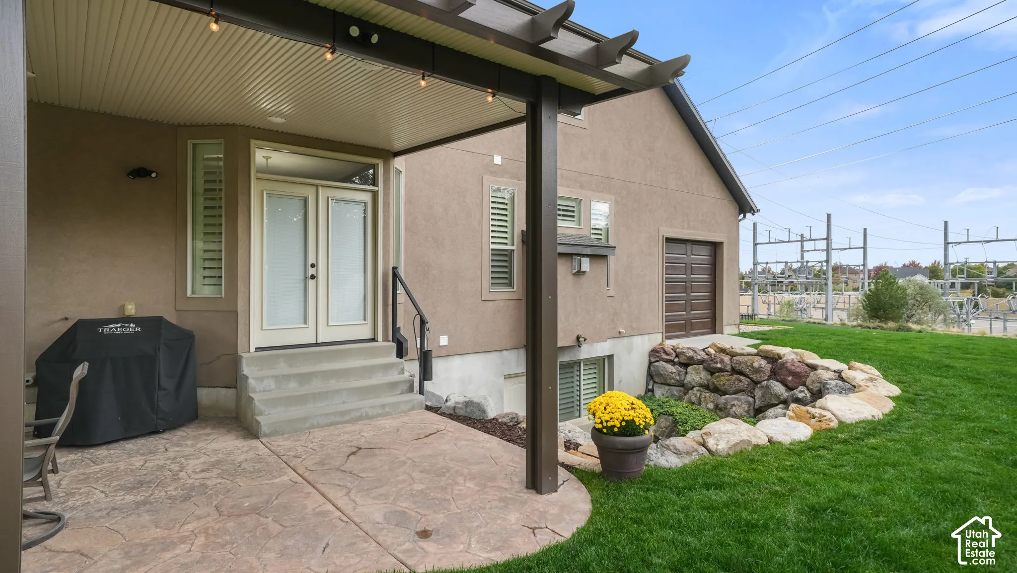 Covered patio with stamped concrete, timber-frame pergola, double-door entrance, and decorative boulder hardscaping