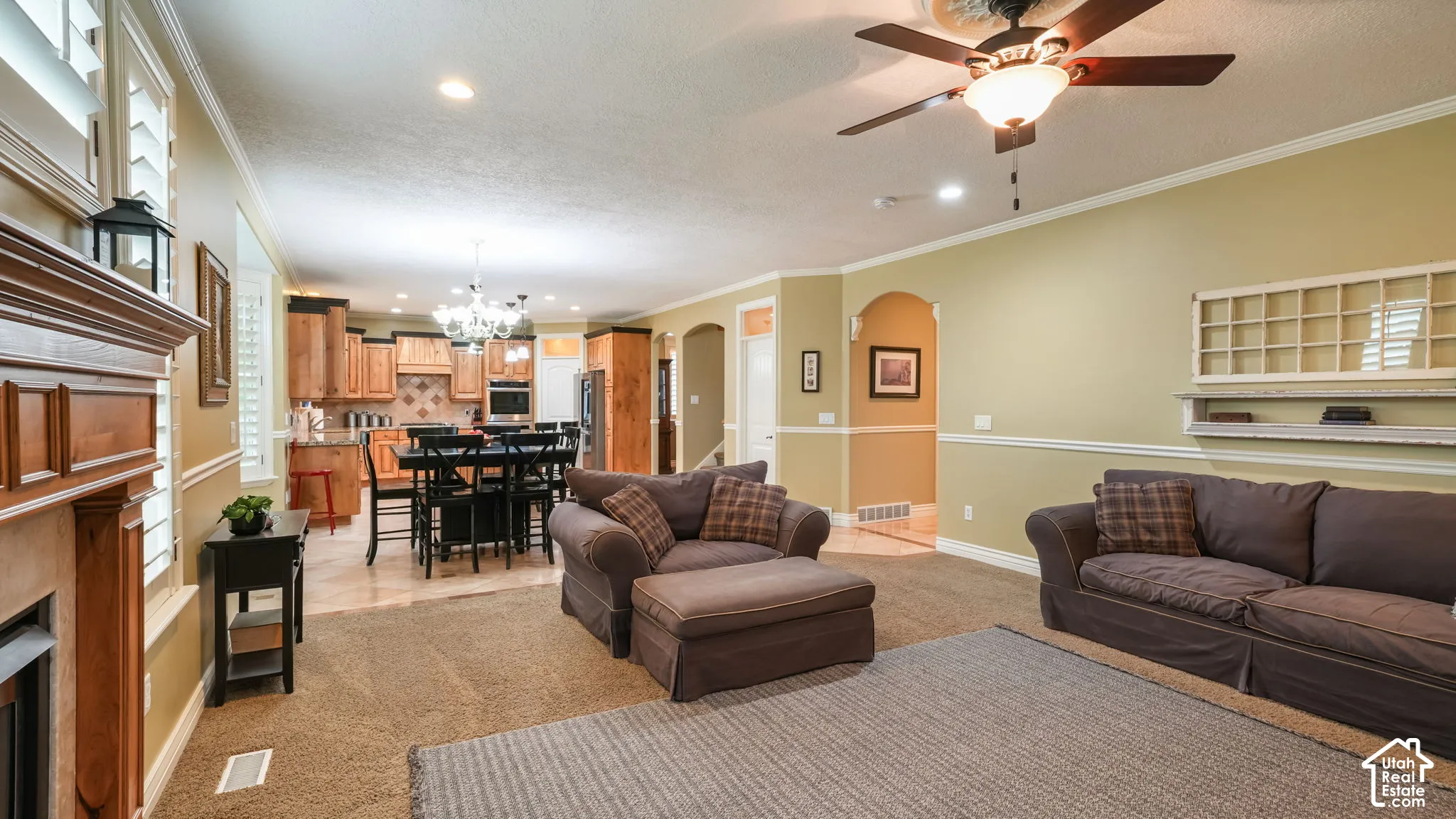 Wood-burning fireplace with a custom wood mantle, crown molding, chair rail trim, overhead ceiling fan with light fixture, and arched interior doorways