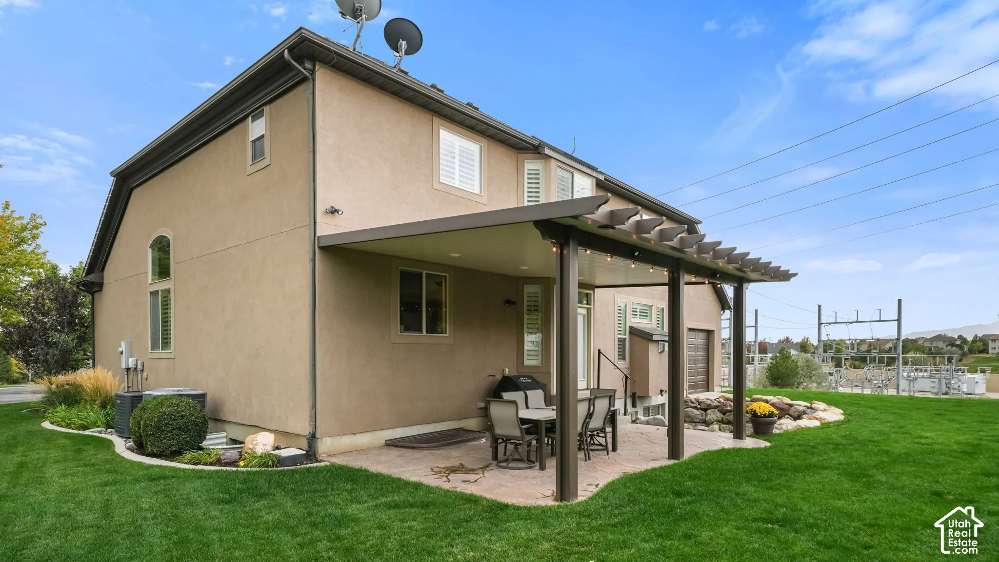 Stucco exterior featuring a covered patio, pergola, stone-edged landscaping, and manicured lawn