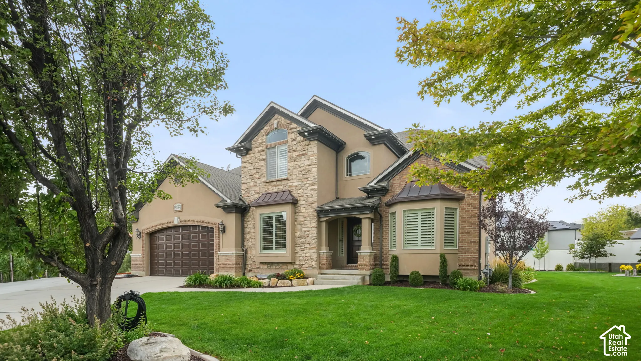 Exterior elevation featuring stone veneer siding, a multi-gabled roofline, metal roof accents, an arched garage door, and a bay window