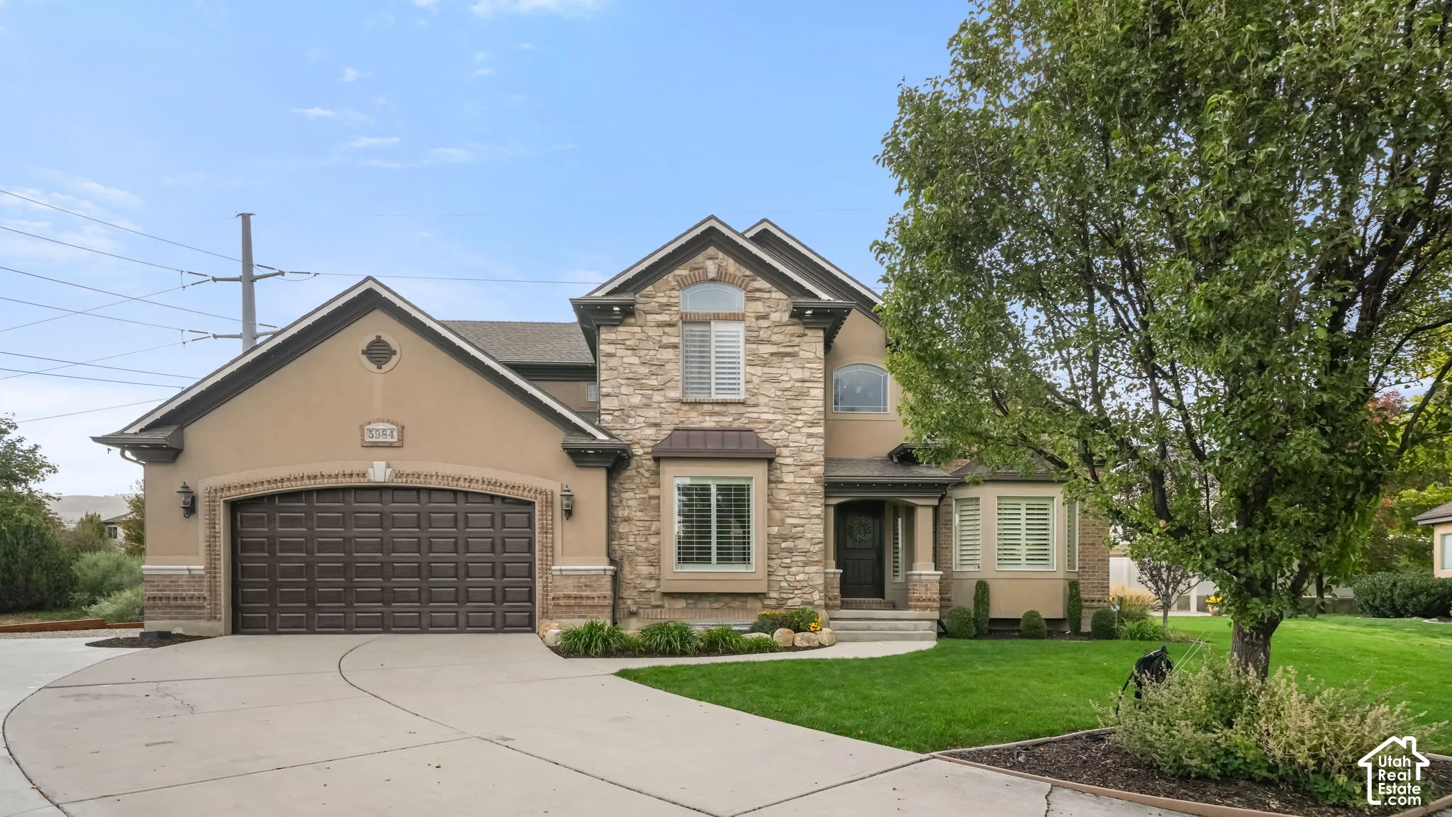 Exterior featuring a multi-gabled facade, stone and stucco siding, a three-car garage, arched brick entryway detailing, and a concrete driveway