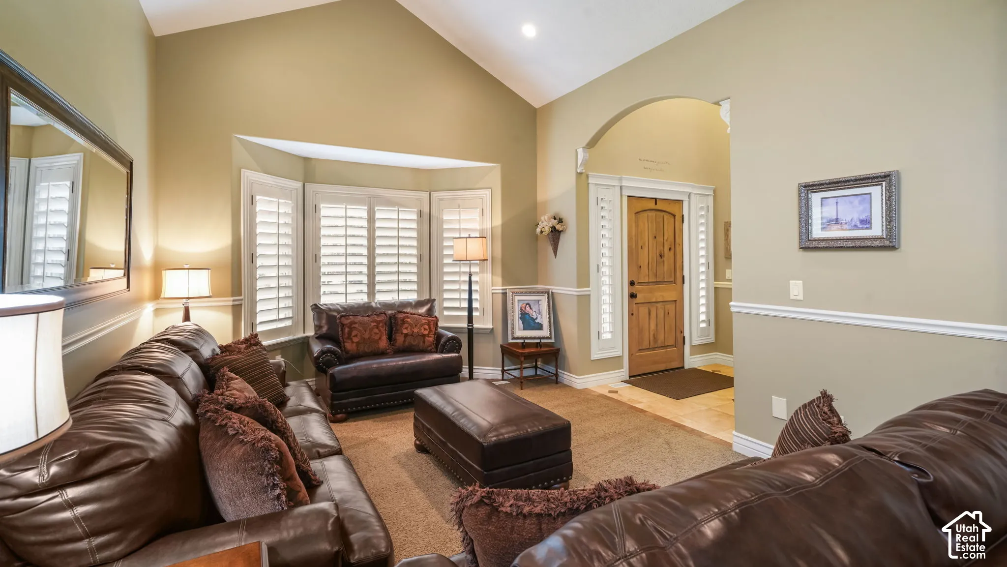 Vaulted ceilings, bay window with plantation shutters, arched entryway, and neutral wall tones with chair rail molding