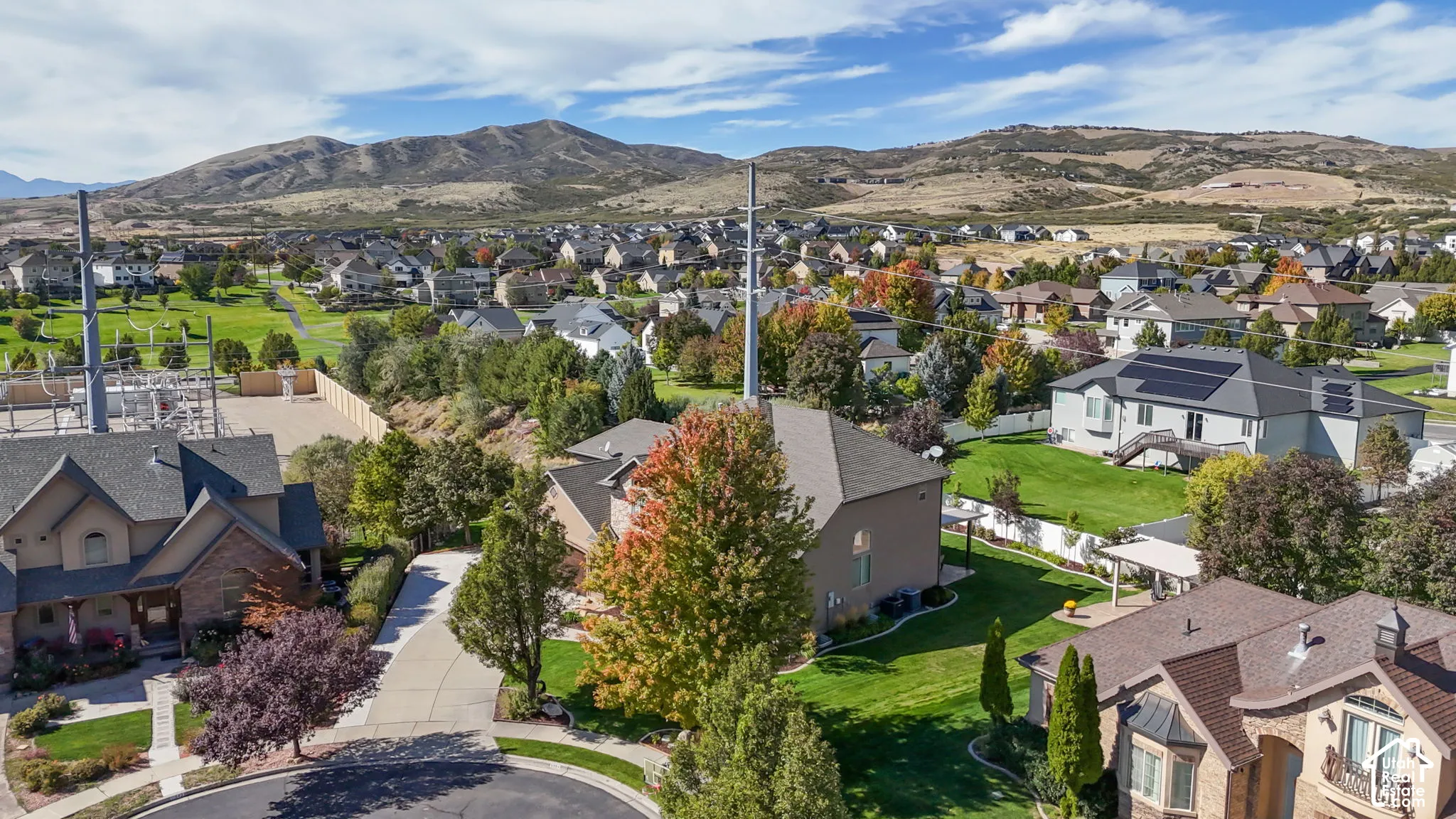 Aerial perspective featuring multi-story residential properties with asphalt shingle roofing, attached garages, and manicured lawns, set against a backdrop of mountain terrain