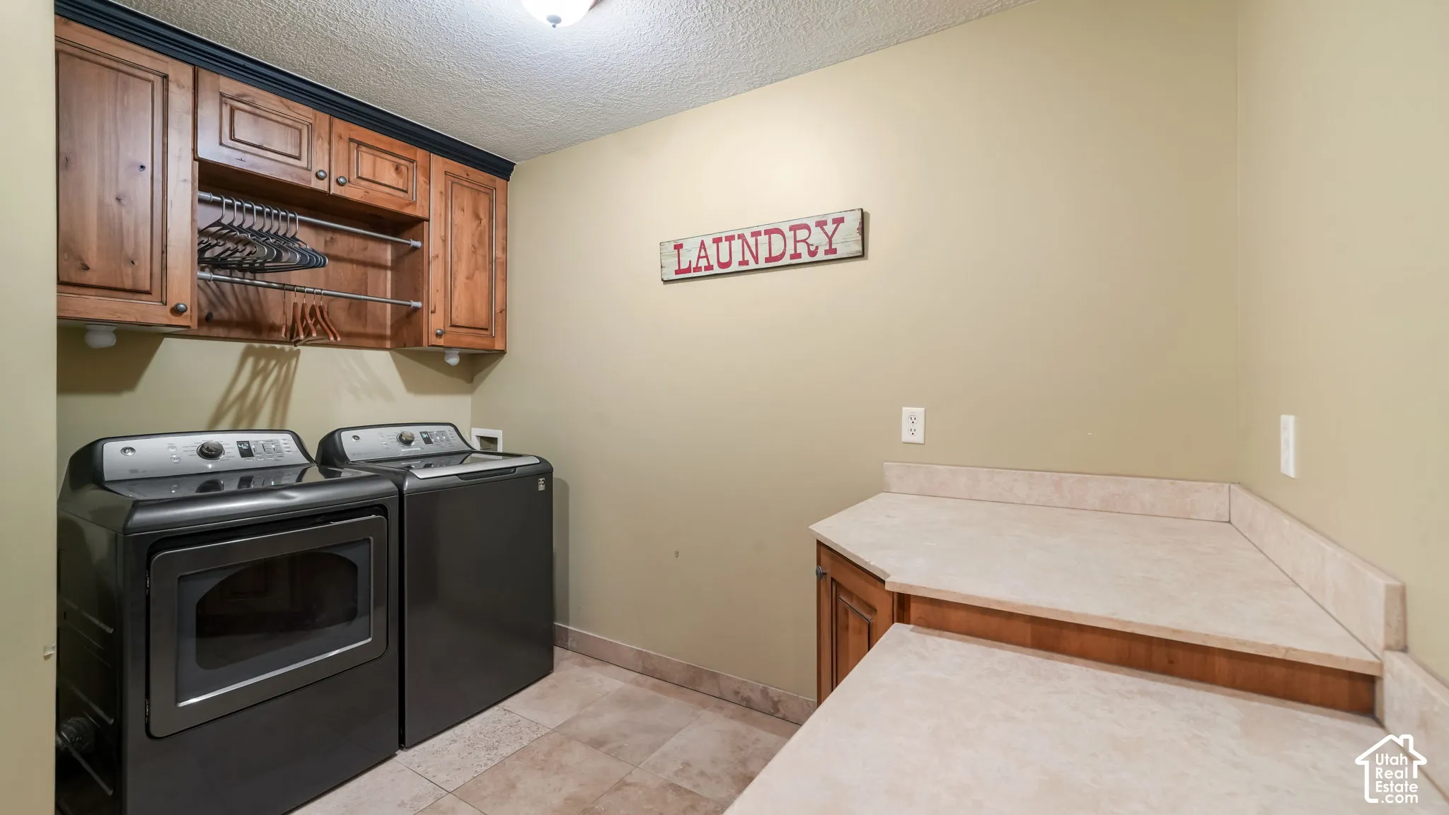 Dedicated laundry space featuring wood-finish cabinetry, integrated garment hanging rod, stone-finish countertops, and tile flooring