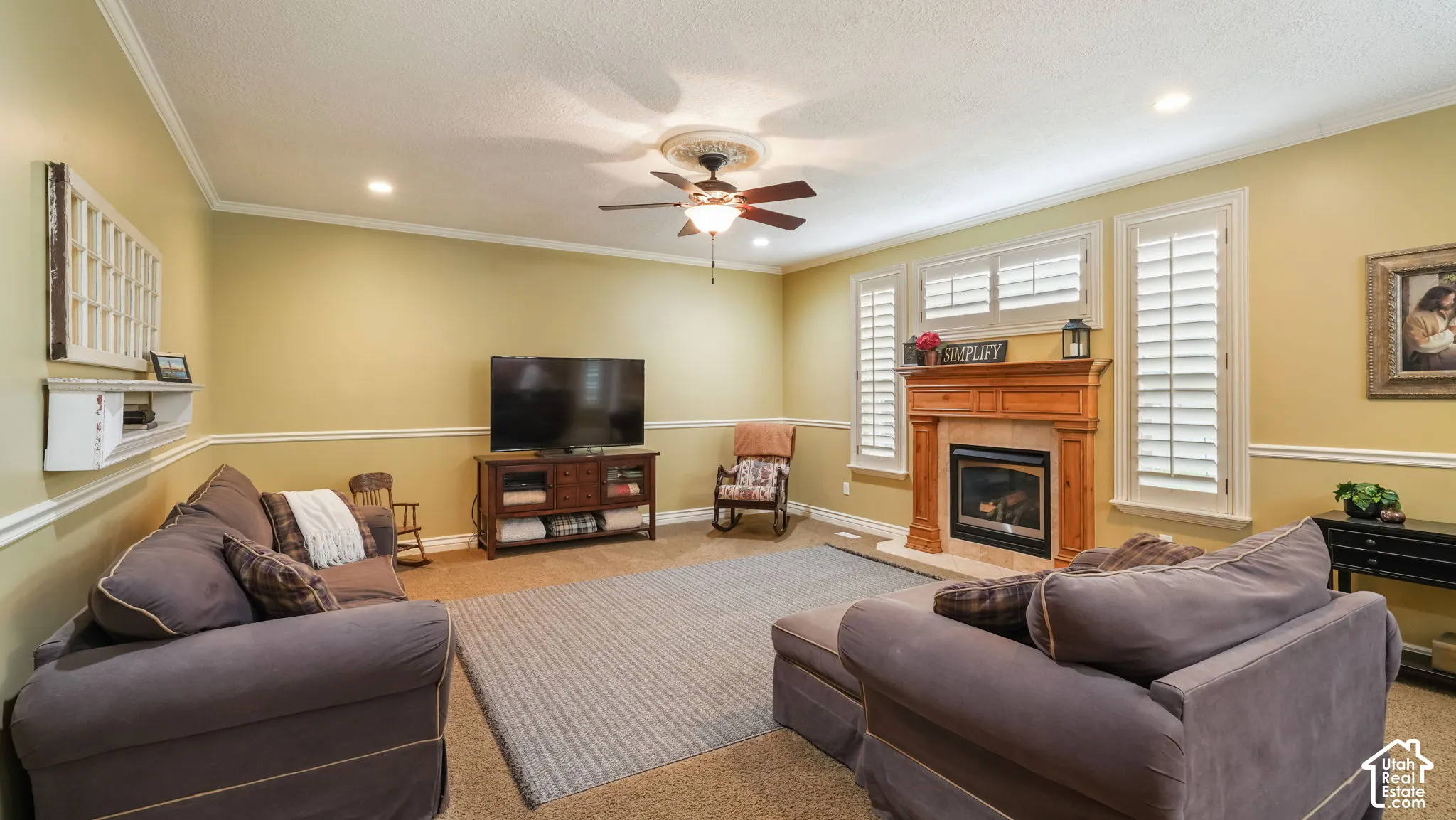 Living area featuring a natural wood fireplace mantel, white interior shutters, recessed lighting, chair rail molding, and a ceiling fan with a medallion