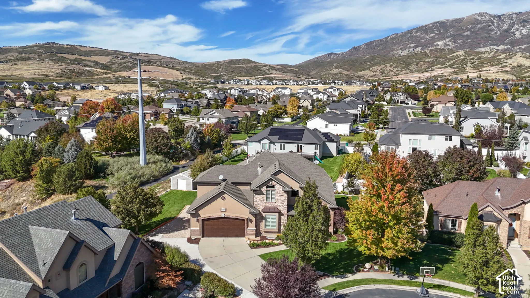 Two-story residence featuring a mixed-material exterior of stone and stucco, a multi-gabled asphalt shingle roof, an attached two-car garage, and established landscaping set against a mountain backdrop
