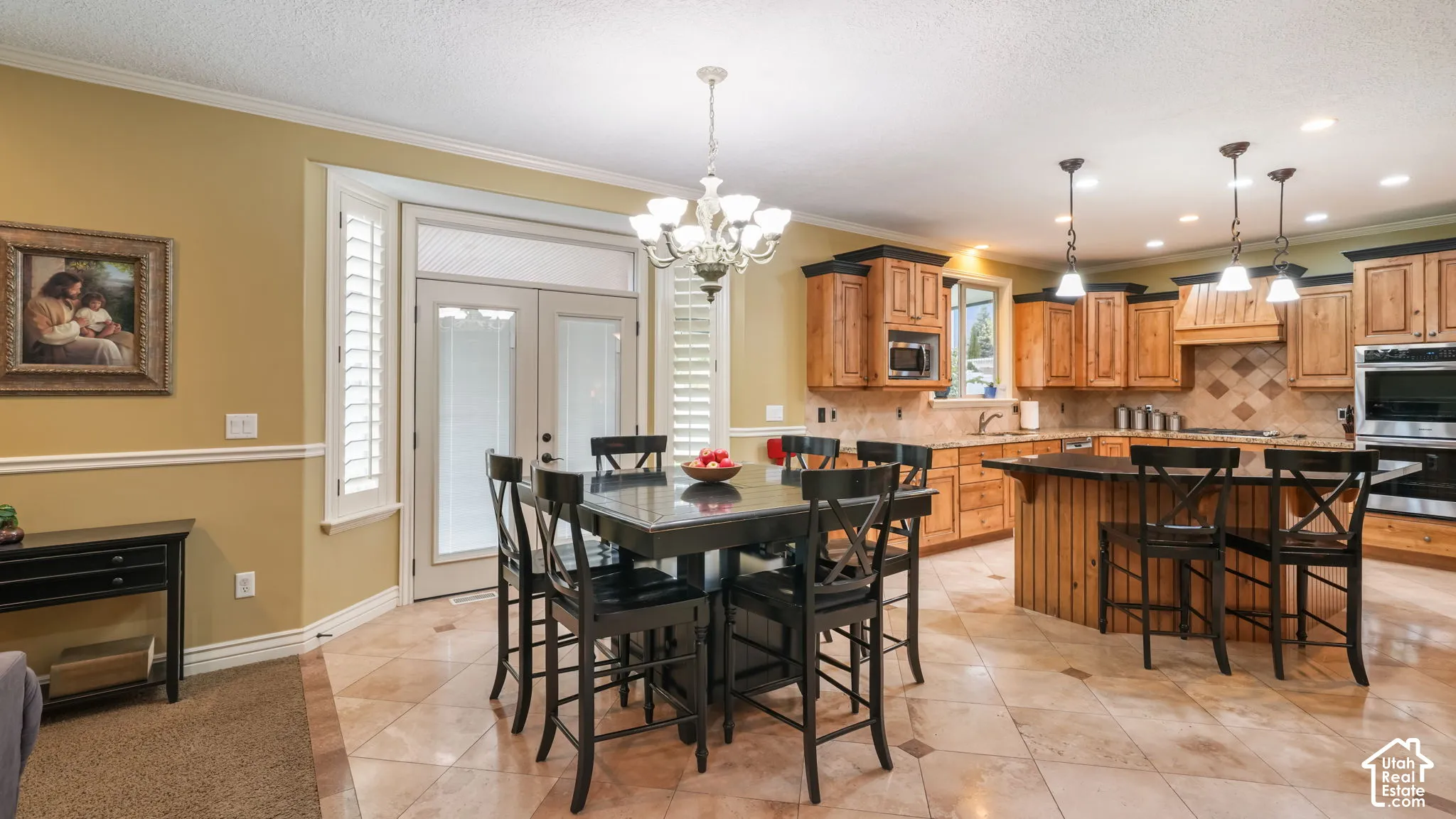Kitchen featuring natural wood cabinetry, stone-finish tile flooring, a tiered center island with stone countertop, built-in double ovens, and glass-paneled double doors