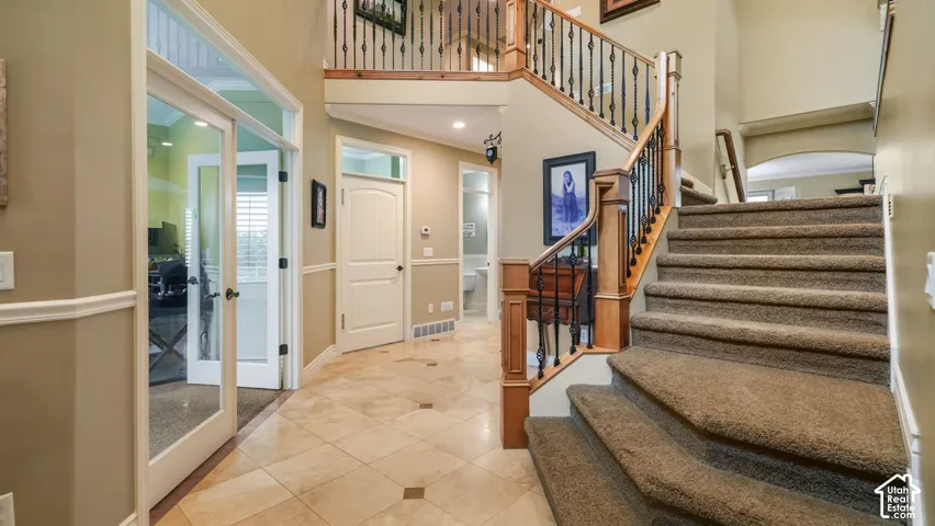 Foyer featuring tile flooring, staircase with wood railings and metal balusters, and glass-paneled double doors